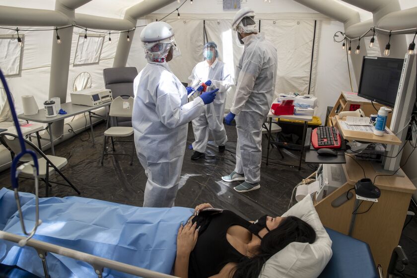 MISSION HILLS, CA - JULY 10: RN Janil Wise (CQ), left, scrub tech Edward Gevshenian, center, and RN Melinda Gruman, right, prepare patient Sarah Bodle, who is pregnant and was exposed to a person with COVID-19, for testing in the OB triage tent at Providence Holy Cross Medical Center on Friday, July 10, 2020 in Mission Hills, CA. (Brian van der Brug / Los Angeles Times)