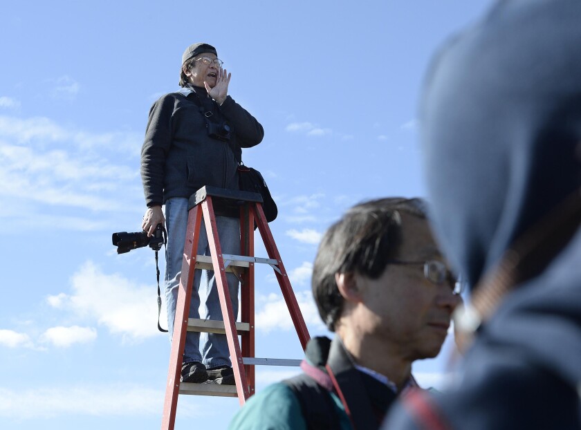 Corky Lee stands on a ladder with a camera in his hand