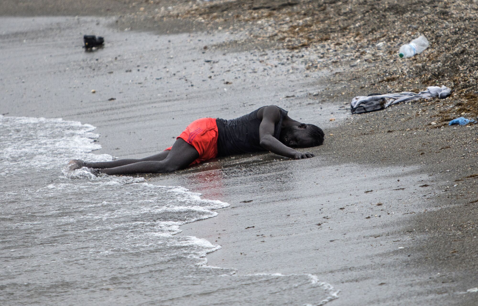 A man lies on the ground on the beach after swimming to the area at the border of Morocco and Spain.
