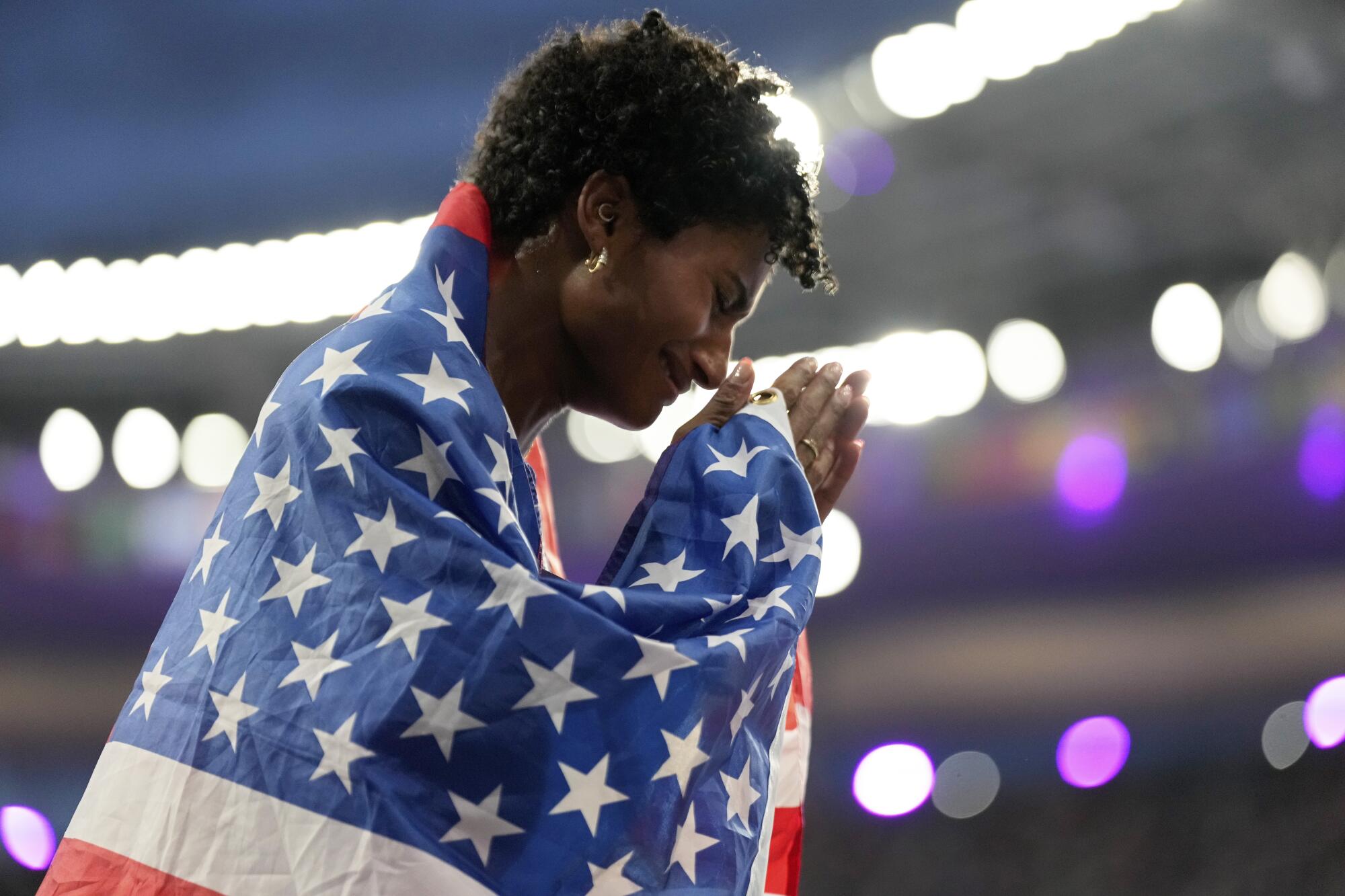 Anna Cockrell from the US clasps her hands while carrying an American flag under bright lights. 