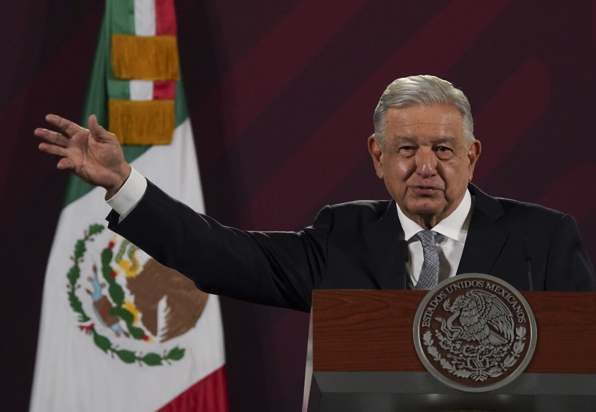 Mexican president Andrés Manuel López Obrador raises a hand at a podium in front of the Mexican flag