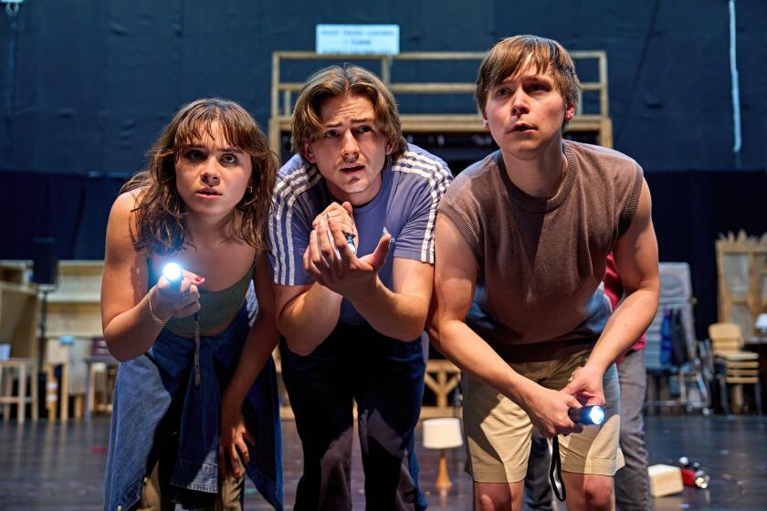 Three teenagers on the set of a play bent forward, holding flashlights.