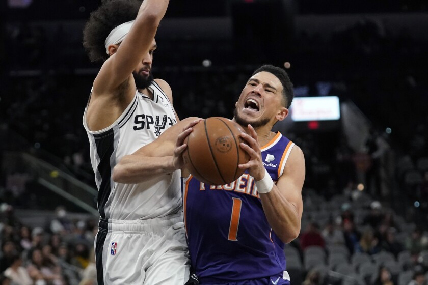 Phoenix Suns guard Devin Booker (1) is fouled as he drives to the basket against San Antonio Spurs guard Derrick White, left, during the second half of an NBA basketball game, Monday, Jan. 17, 2022, in San Antonio. (AP Photo/Eric Gay)