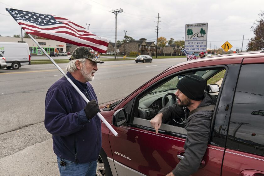 A passing motorist at right argues with Trump supporter Mike Jamerson, left, during a rally at an intersection in Mount Clemens, Mich., Thursday, Oct. 29, 2020. As the traditional Election Day closes in, Americans are exhausted from constant crises, on edge because of volatile political divisions and anxious about what will happen next. (AP Photo/David Goldman)