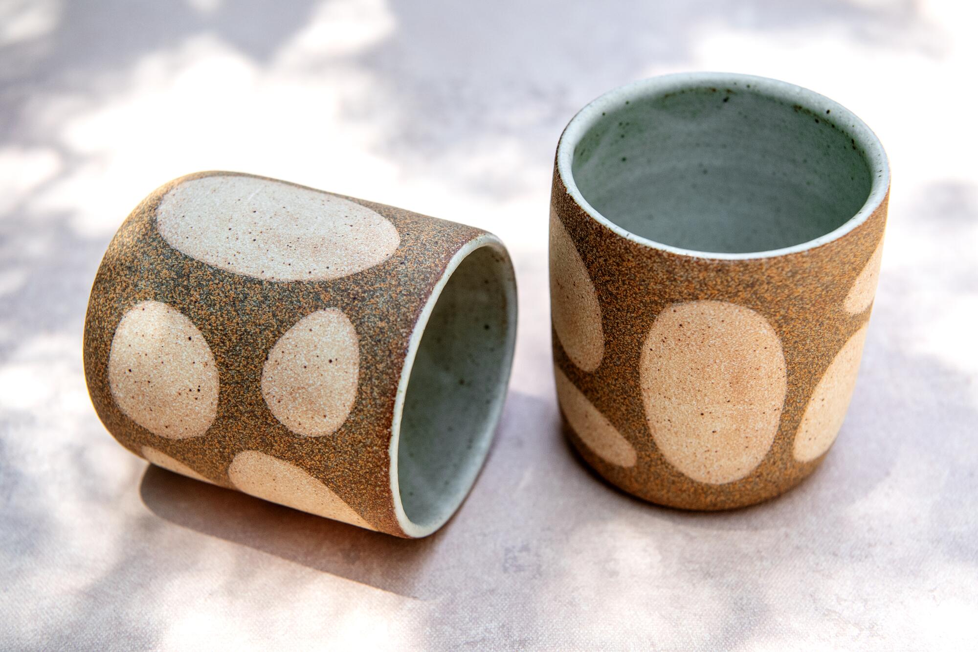 Two small clay cups with ovals on the outside.