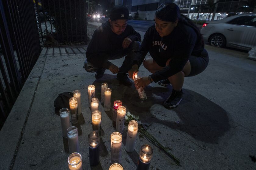 LOS ANGELES, CA - December 19 2021: A couple light candles at a makeshift memorial on Martin Luther King Jr. Blvd. on Martin Luther King Jr. Blvd. in honor of slain rapper Drakeo the Ruler on Sunday, Dec. 19, 2021 in Los Angeles, CA. (Brian van der Brug / Los Angeles Times