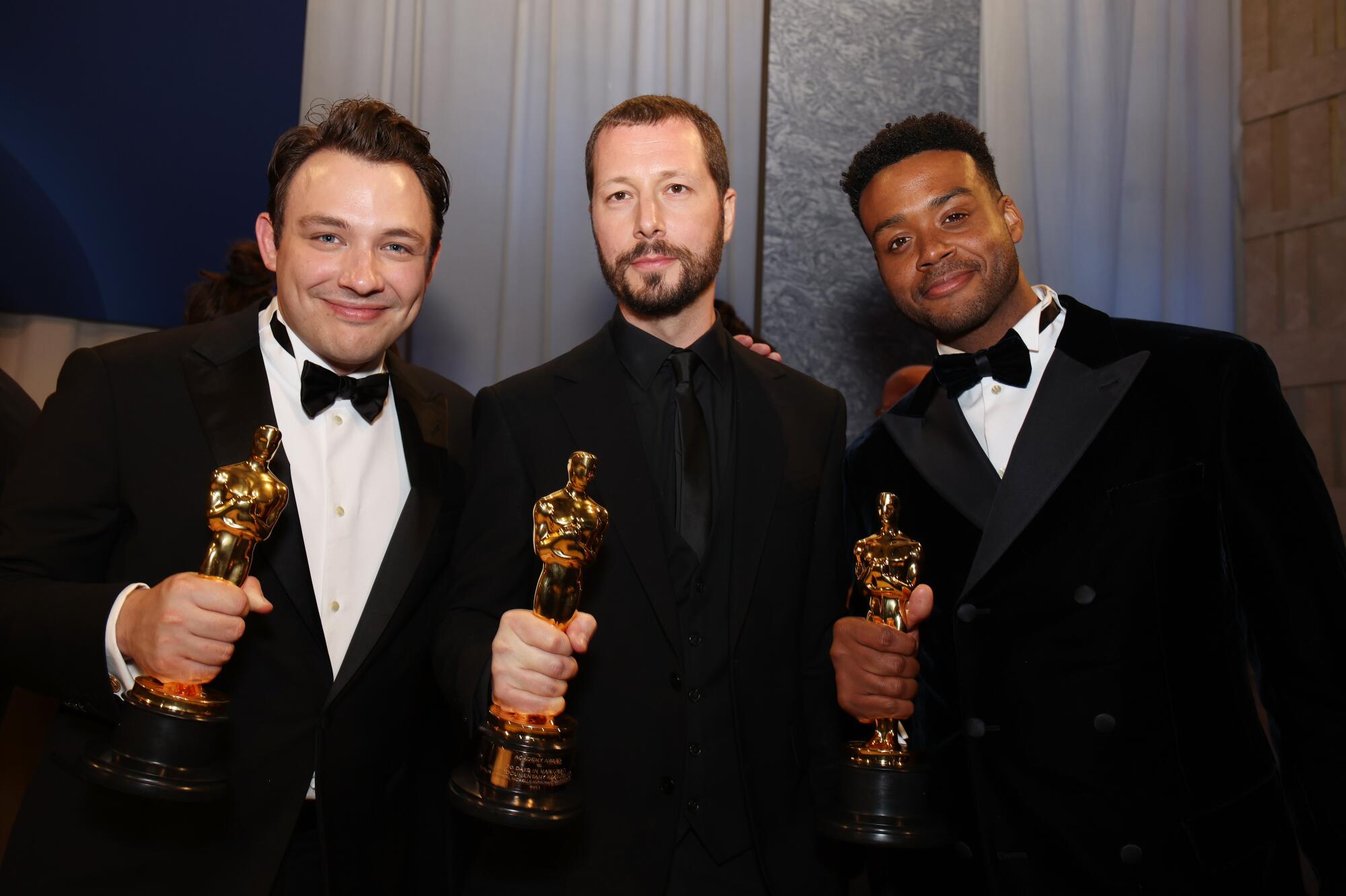 Three men holding Oscars smile for the camera.