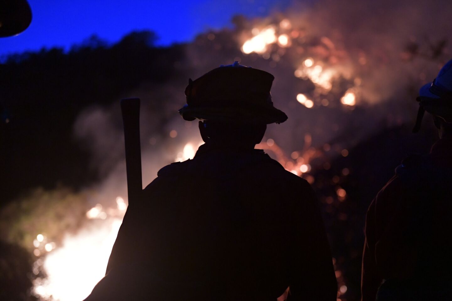 An L.A. County inmate fire crew member is outlined by the glow of flames at the Fish fire Monday.