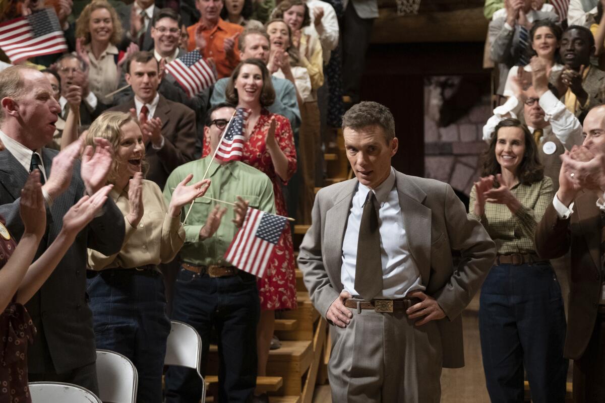 Cillian Murphy's Robert Oppenheimer stands in a crowd of people waving U.S. flags in "Oppenheimer"