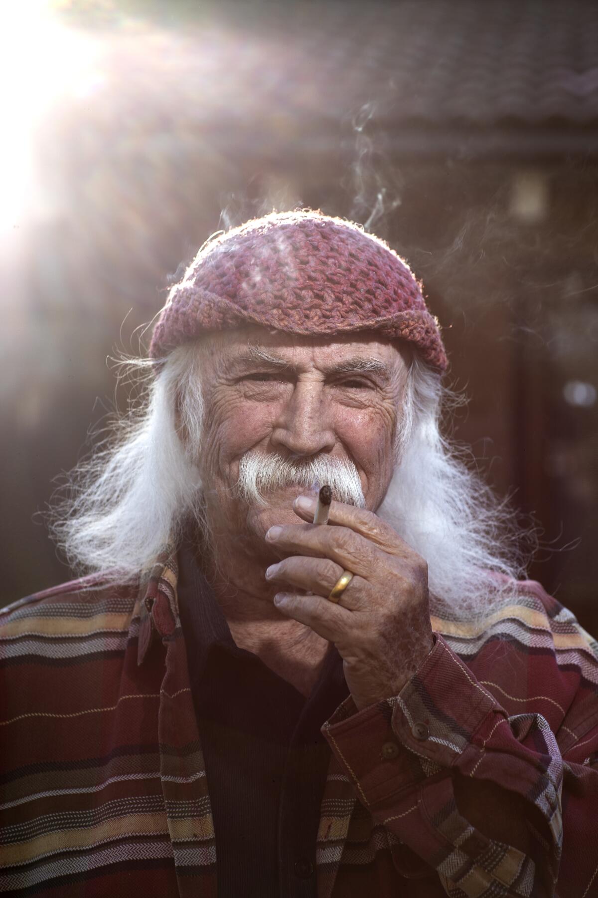 A man with long white hair and a mustache, smoking a cigarette