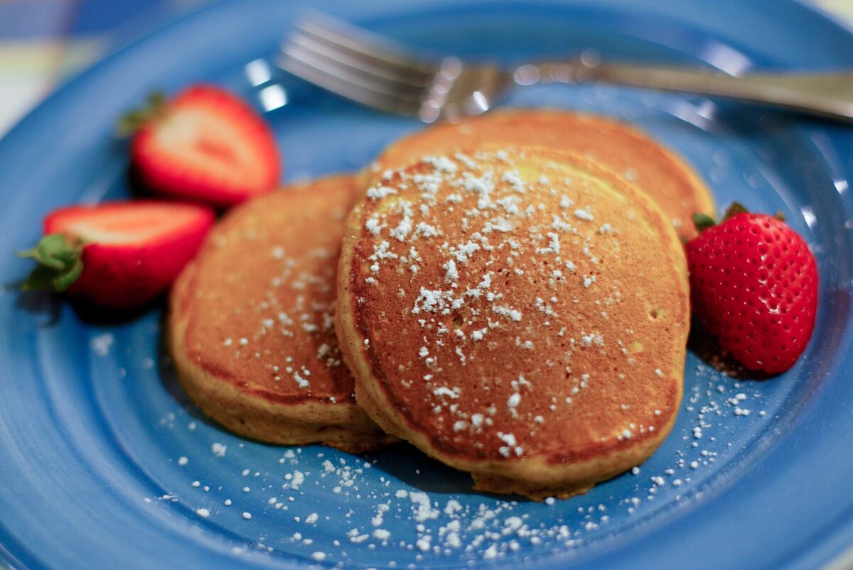 Small pancakes on a blue plate are sprinkled with powdered sugar, with two strawberries on the side.