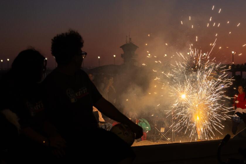 Huntington Beach, CA - July 04: People watch fireworks explode at dusk near the pier before the official fireworks show over the pier and ocean in Huntington Beach. Thousands of people celebrated Independence Day, 4th of July in Huntington Beach Thursday, July 4, 2024. (Allen J. Schaben / Los Angeles Times)
