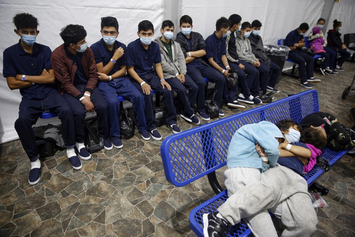 ARCHIVO - varios adolescentes y niños migrantes esperan su turno en un sitio de procesamiento