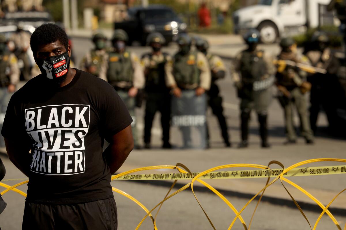 A protester stands close to sheriff's deputies near the South L.A. Sheriff's Station protesting fatal shootings.