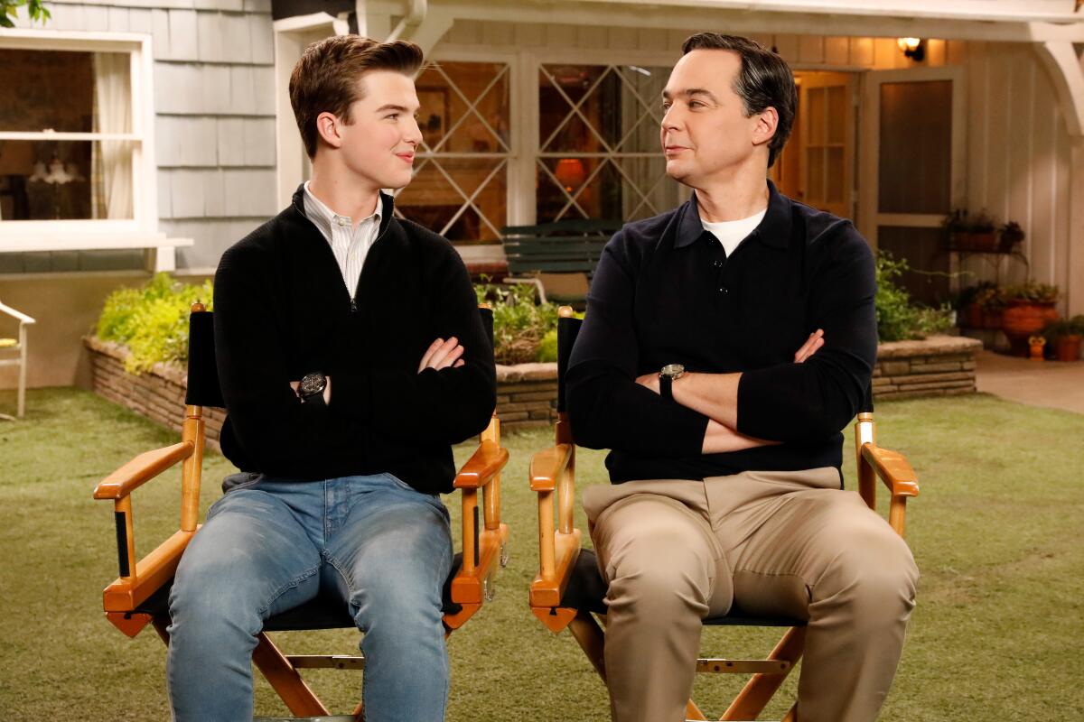 Iain Armitage, left, and Jim Parsons sitting in directors' chairs on a TV set looking at one another.