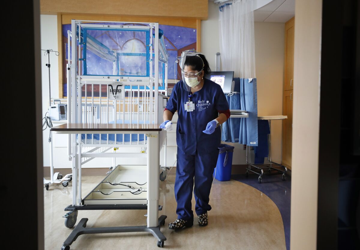 A woman in blue scrubs cleans a hospital room