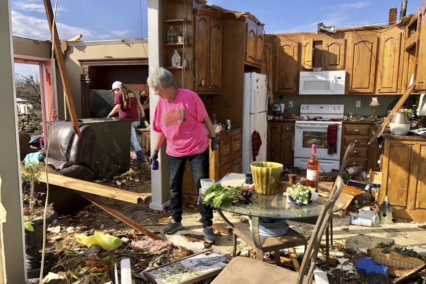 A woman sorts through the remains of a house with its roof gone.