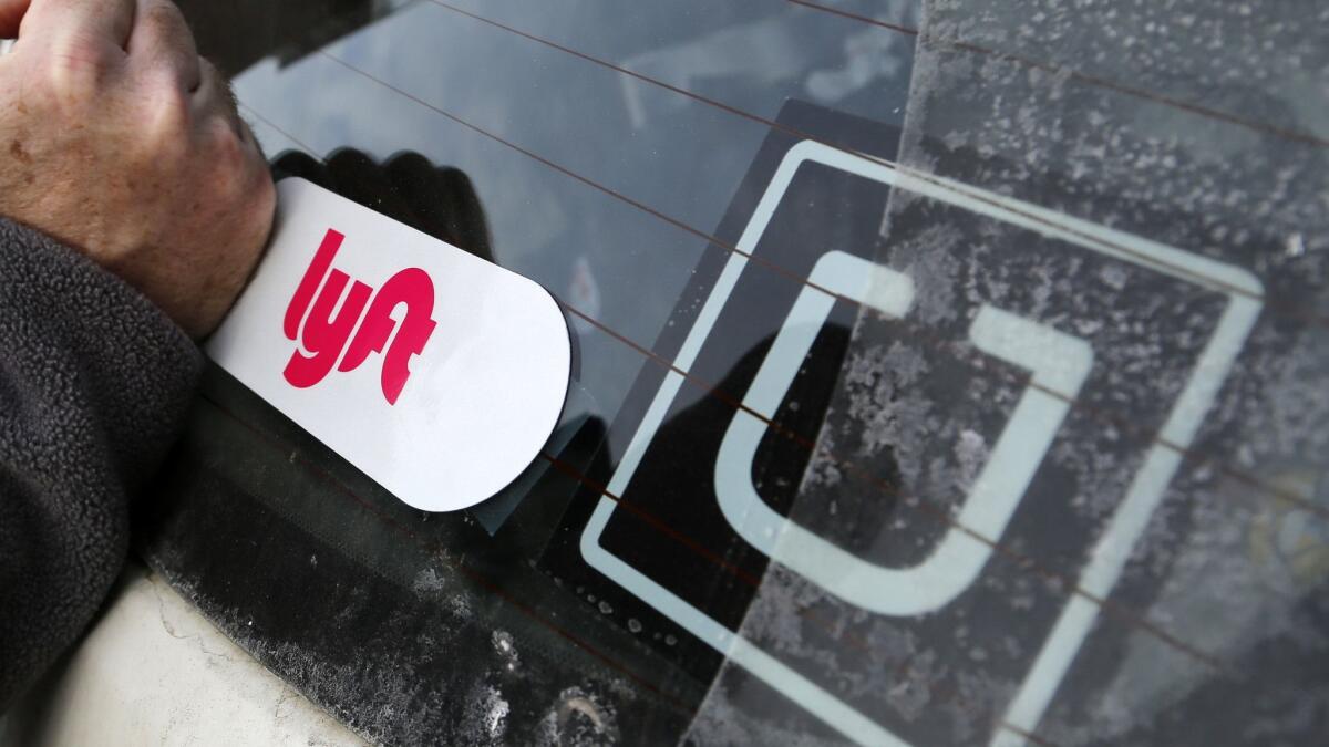 A person smooths a Lyft logo next to an Uber sticker on the rear window of a car.