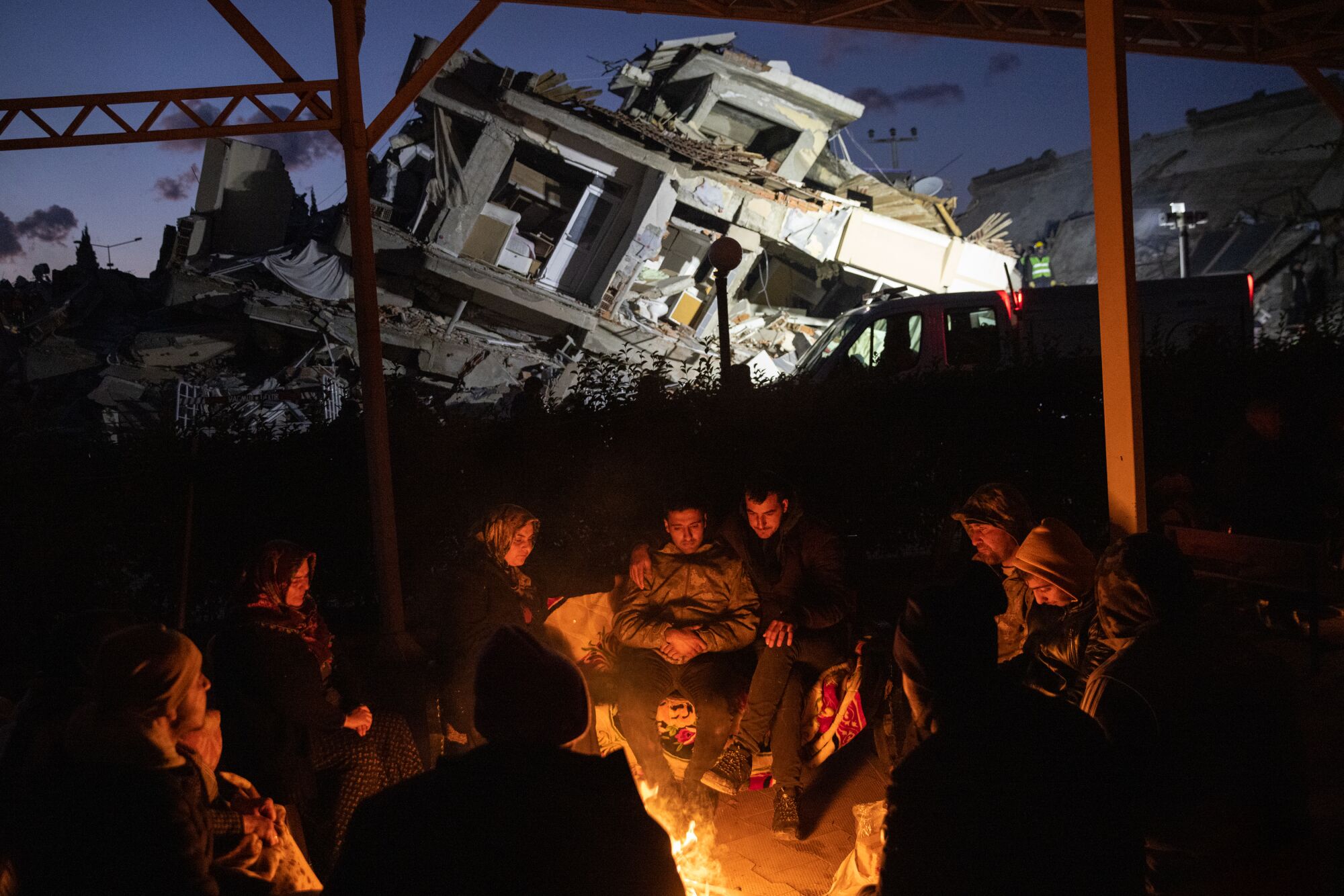 People warm up by a fire amid the rubble of destroyed buildings