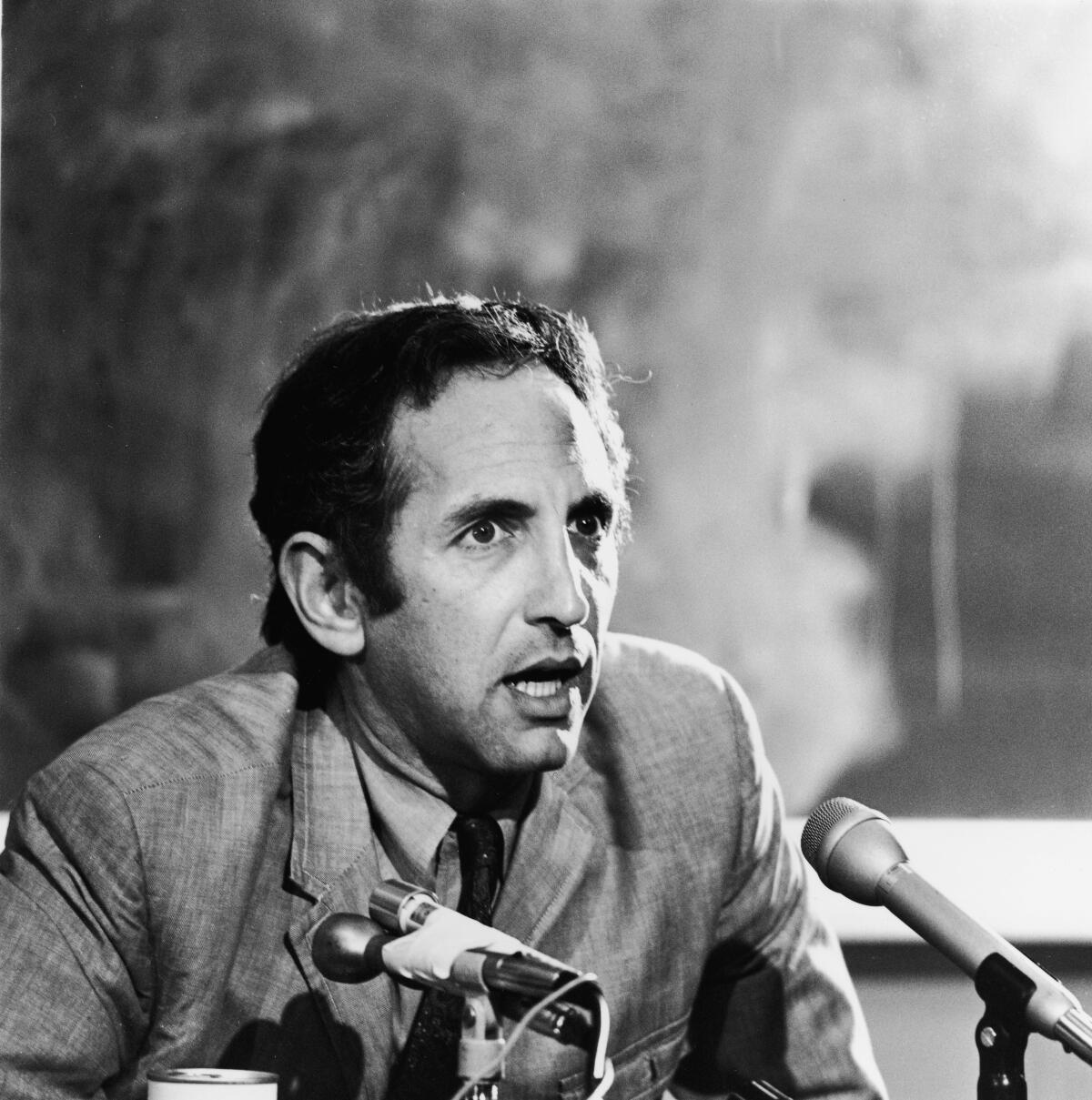 A black-and-white photo of a man speaking into two microphones.