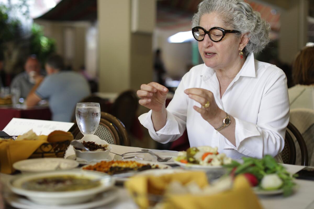 A woman in a white blouse eats at a restaurant table.