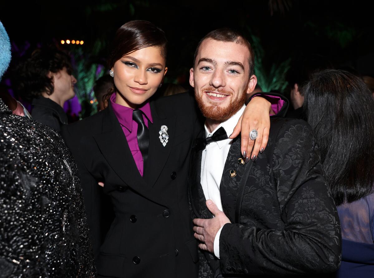 Zendaya wearing a black and purple suit embracing and posing with Angus Cloud in a black tuxedo