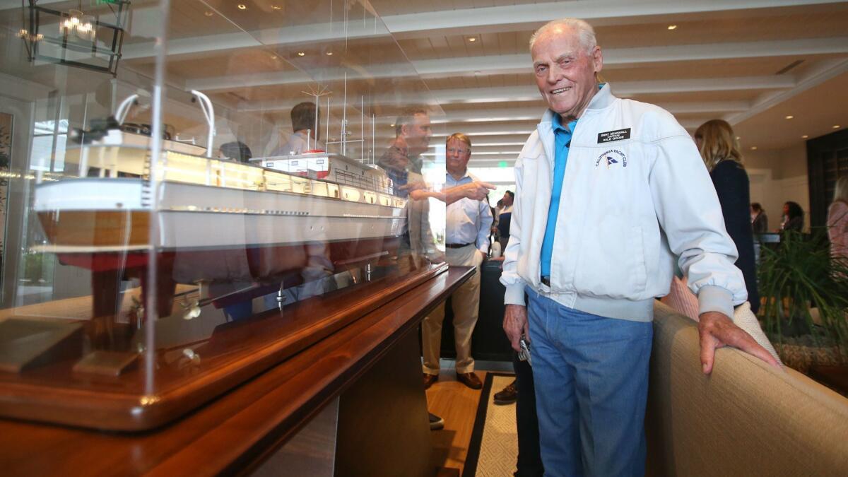 Bert Minshall, captain of John Wayne’s yacht, Wild Goose, during its heyday, stands next to the new model of it in the lobby of the Lido House hotel in Newport Beach.