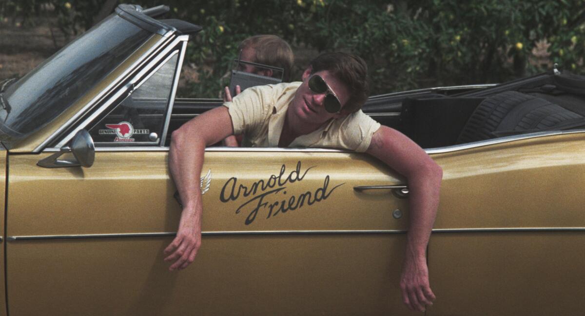 A man in sunglasses leans with both arms over the side of a convertible. On the care are the words "Arnold Friend."