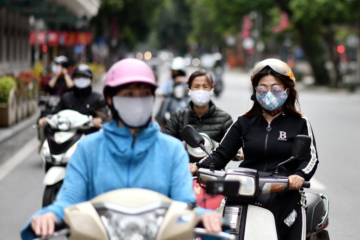 Motorists in masks wait at a stoplight in Hanoi, Vietnam