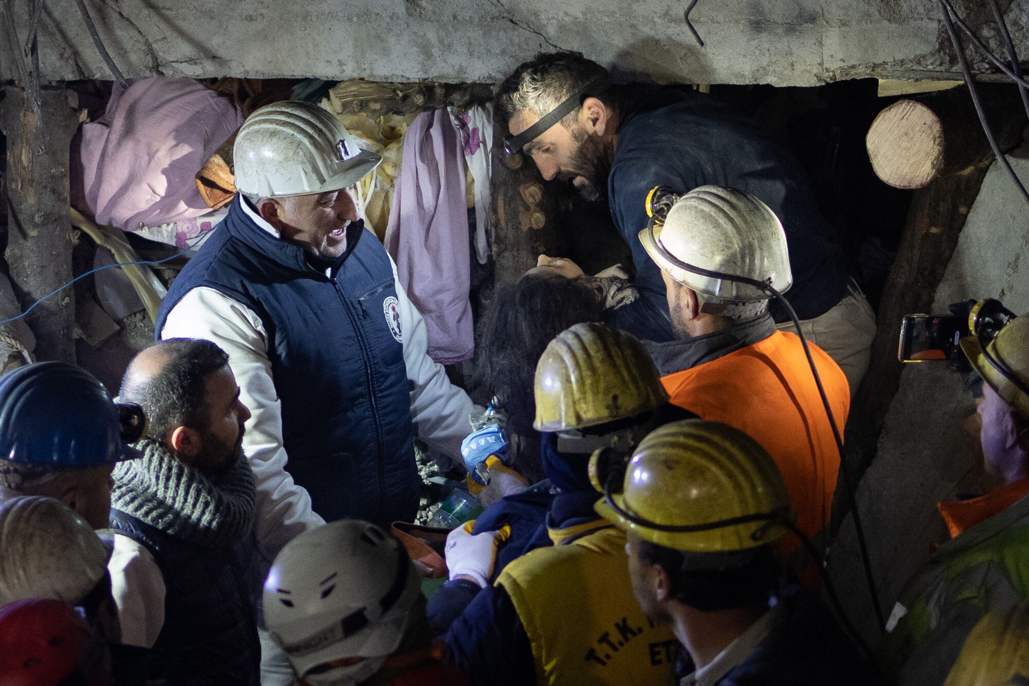 Des gens portant des casques et des lampes frontales travaillent au milieu des décombres la nuit.