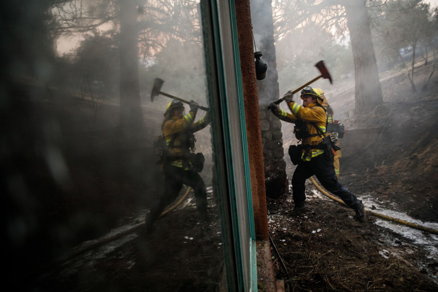 A Contra Costa County firefighter breaks a wall with an ax as his crew battles flames inside a home along Highway 29 north of Calistoga on Oct. 12.