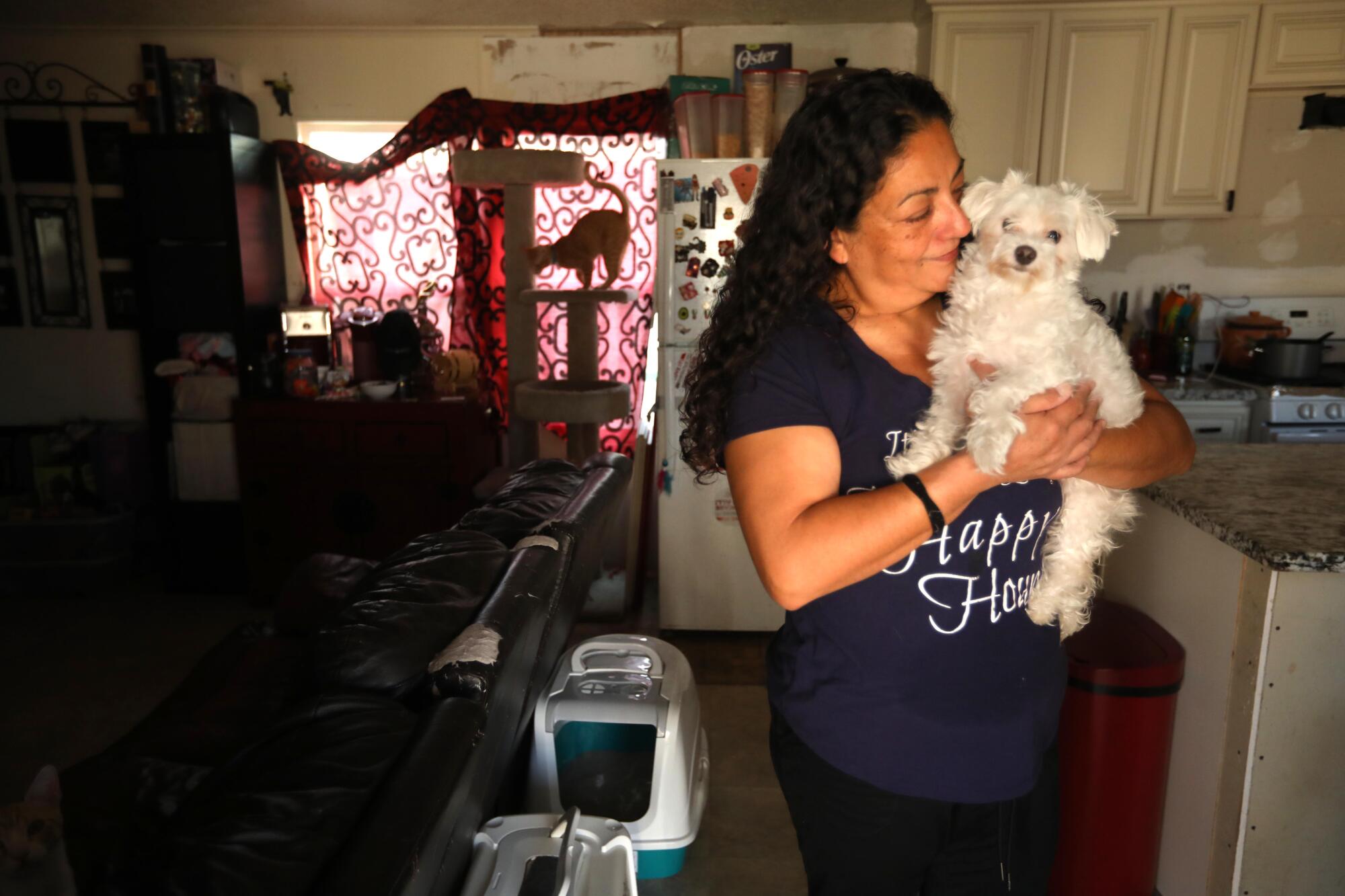 A woman holds a small white dog inside a home 