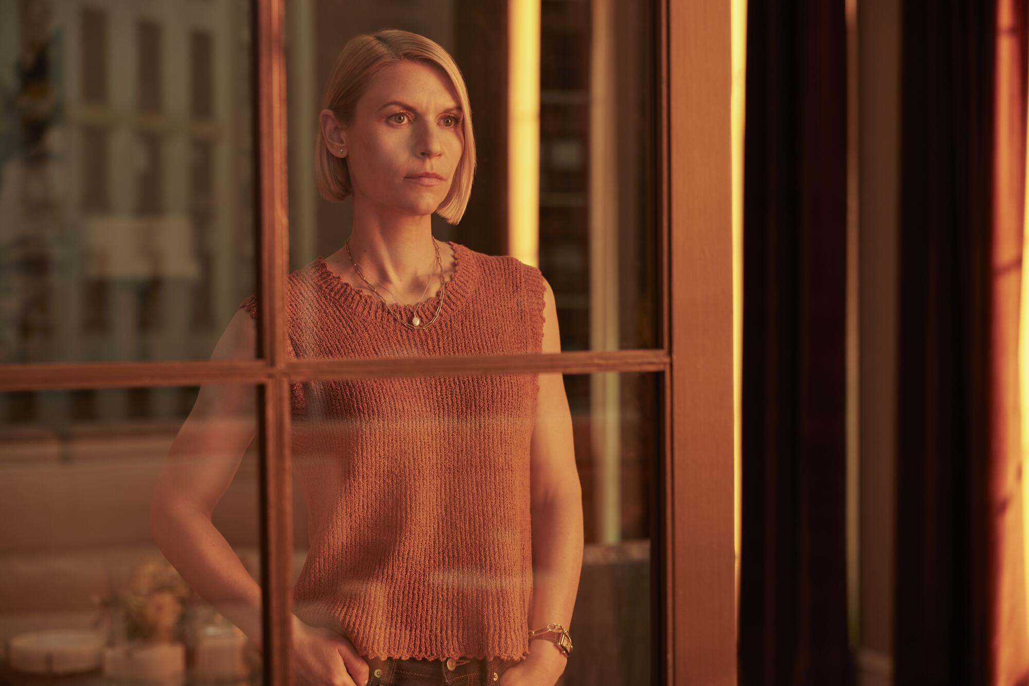 A woman with short blond hair looks at her reflection in a glass door.