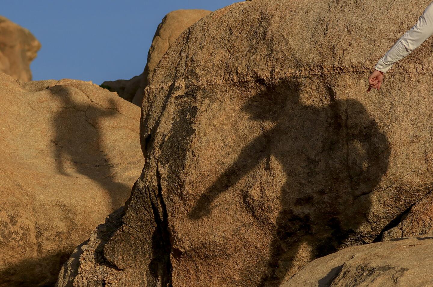 The climbers' shadows are cast on the boulders at "Trash Can Rock" at sunset in Joshua Tree National Park.