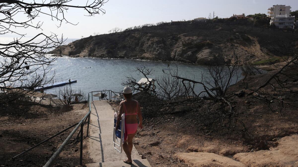 A woman walks towards a beach in Rafina, east of Athens, on Wednesday, 10 days after deadly wildfires blackened the seaside resort.