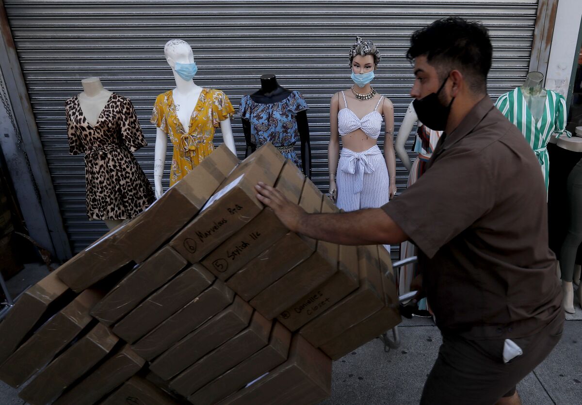 A masked deliveryman moves packages past mannequins wearing similar facial coverings in the garment district in downtown L.A.