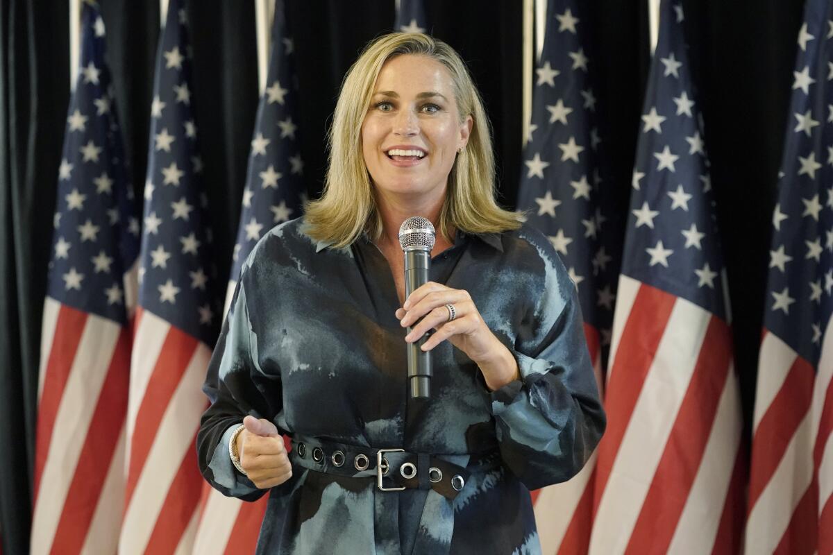 Senate candidate Tiffany Smiley speaks into a microphone in front of a backdrop of American flags. 