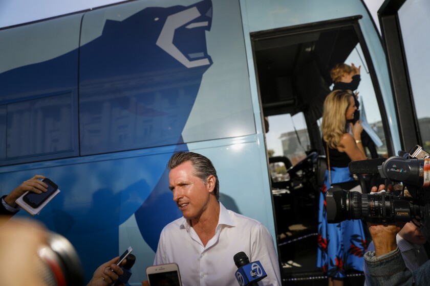 Gavin Newsom speaks with a media gaggle in front of a tour bus