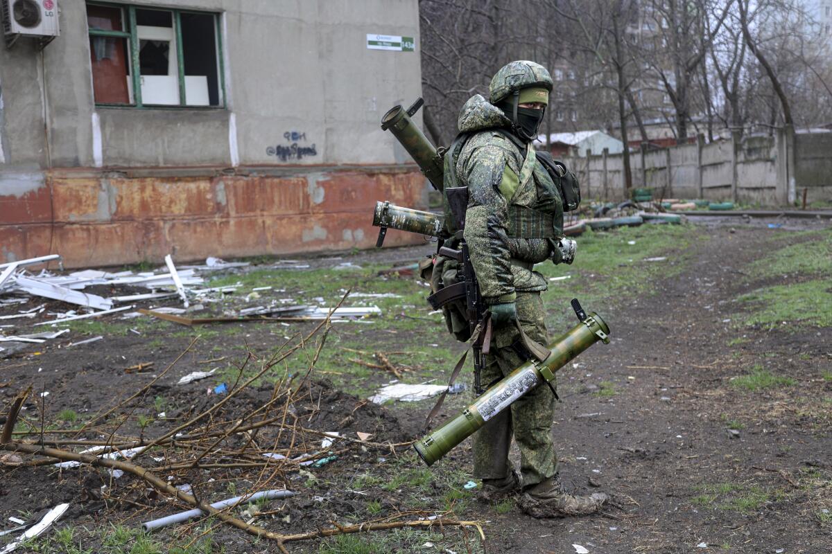 A heavily armed militia member walks through a debris-filled yard in Mariupol.