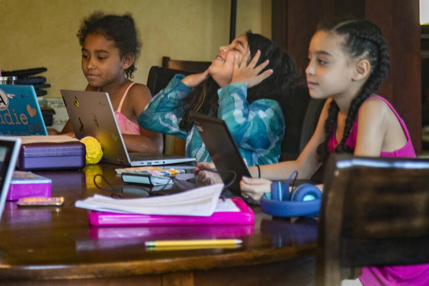 RIVERSIDE, CA- APRIL 23, 2020: Rosie Roth, middle takes a breather from typing class seated next to Andie Bristow, left and Allison Furbush, right, at the Bristow's dining room table during home school in the midst of the coronavirus pandemic on April 23, 2020 in Riverside, California. The Bristow's, Roth's and Furbush's, who are also neighbors, have quarantined together and are home schooling the 8 children amongst them using the parents as teachers. They've named the school "Brothbush Academy" coined from the families' last names.(Gina Ferazzi / Los Angeles Times)