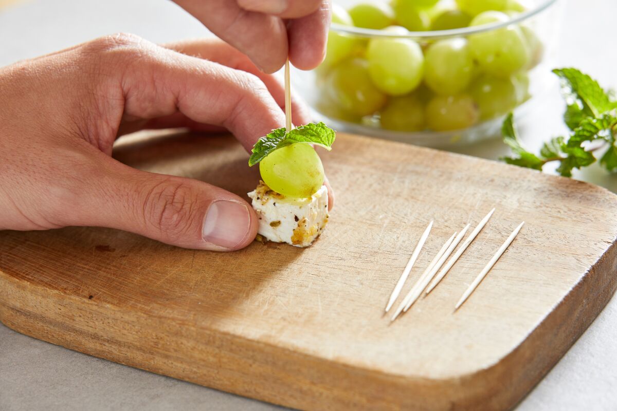 A skewer is assembled with a mint leaf, grape and marinated feta.