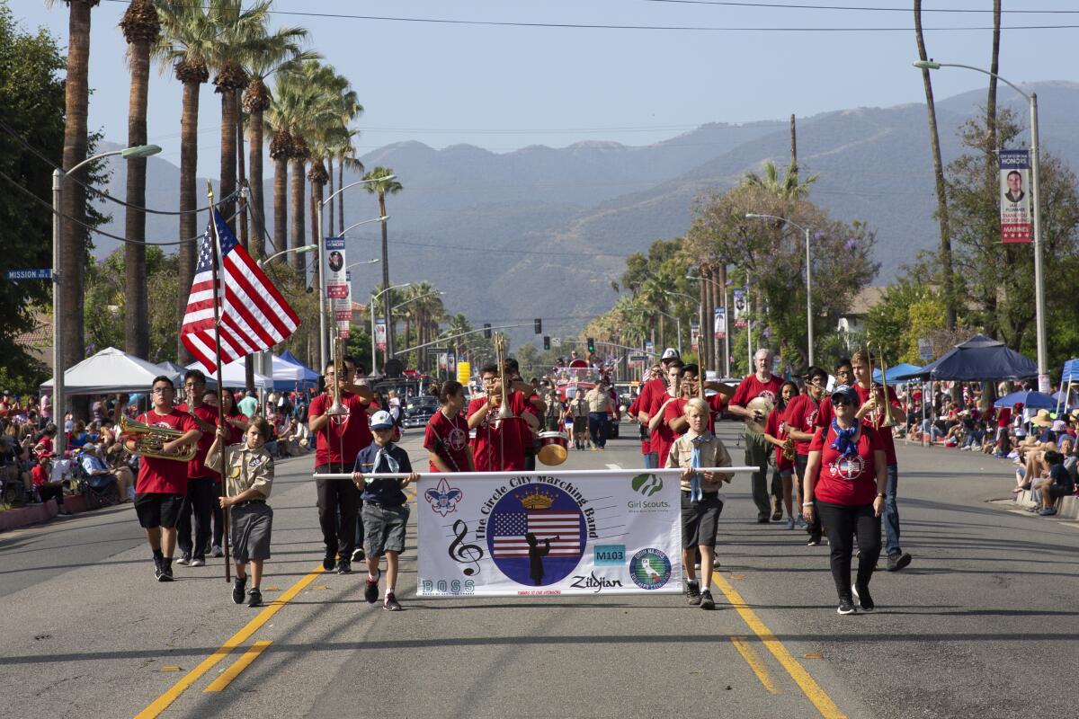 People march down a street lined with palm trees, holding a banner with mountains in the background. 