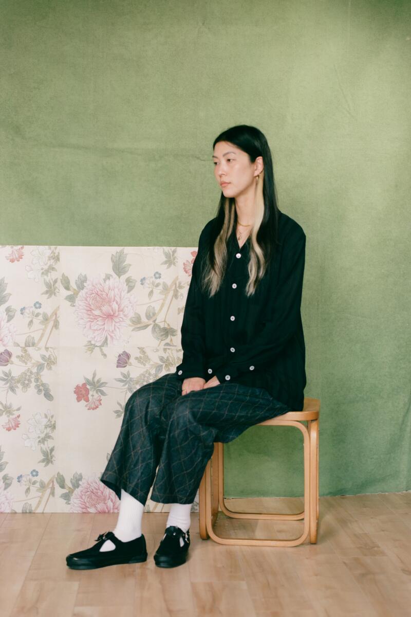 Julia sits on a stool in front of a green and floral backdrop