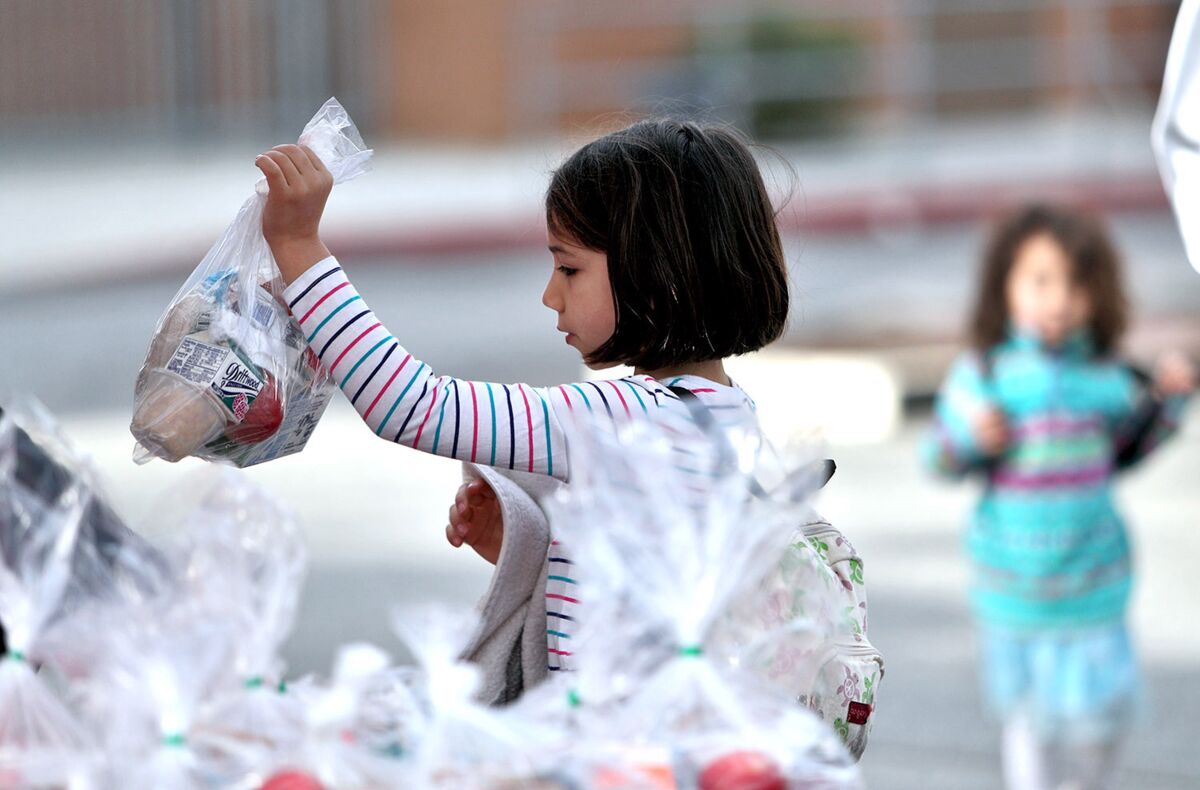 Chelsea Simmons, a 7-year-old first-grader, grabs her breakfast and lunch bag in the Glendale High School parking lot distribution area during Glendale Unified's new grab-and-go drive-up meal service on Tuesday.