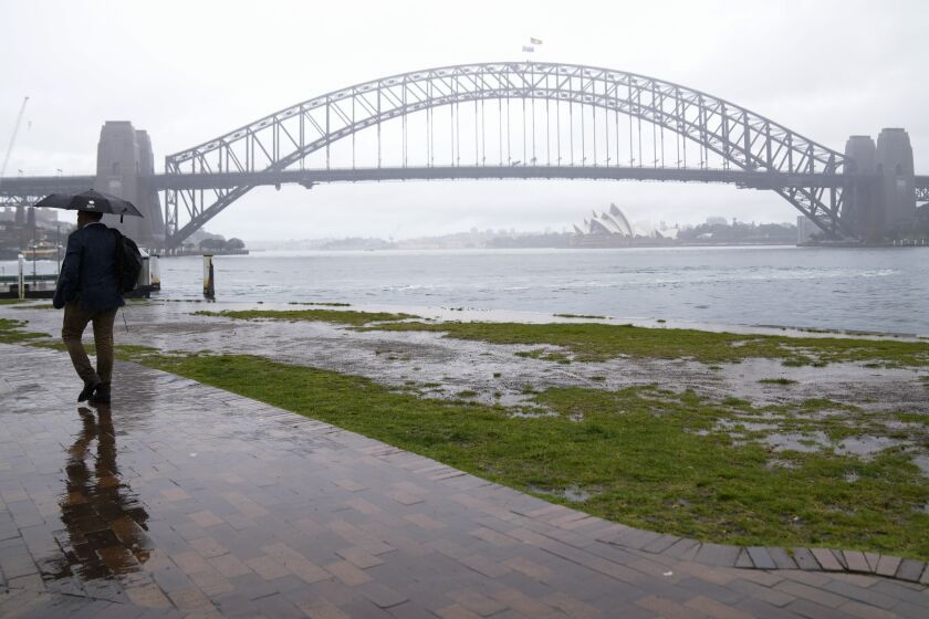 A commuter waits in the rain in Sydney, Australia, Thursday, Oct. 6, 2022. Sydney notched up its wettest year in over 160 years of records, Weatherzone's Andrew Miskelly said, recording 2199.8mm at 1.10pm. The previous record was 2194mm in 1950. (AP Photo/Mark Baker)