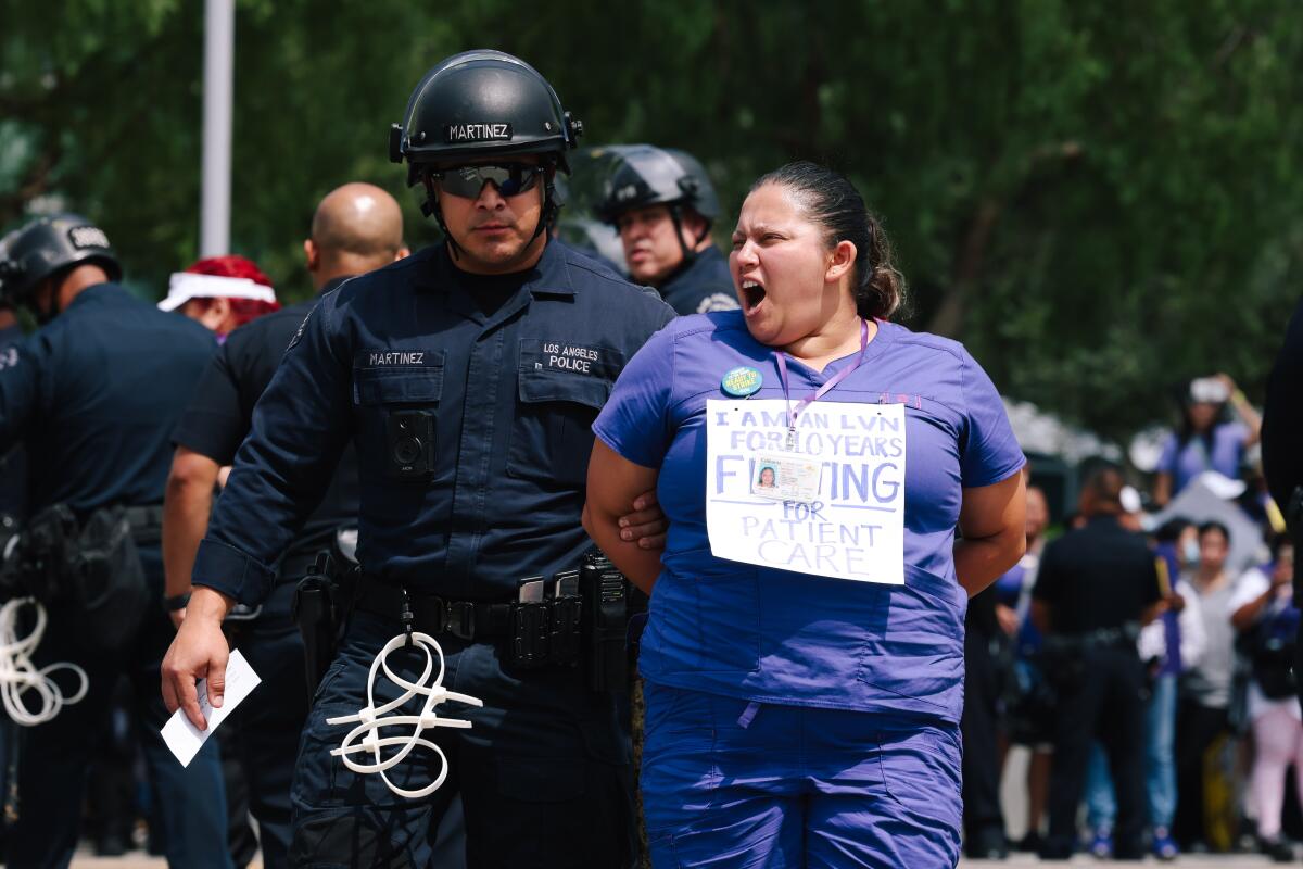 A police officer leads a handcuffed person in scrubs.