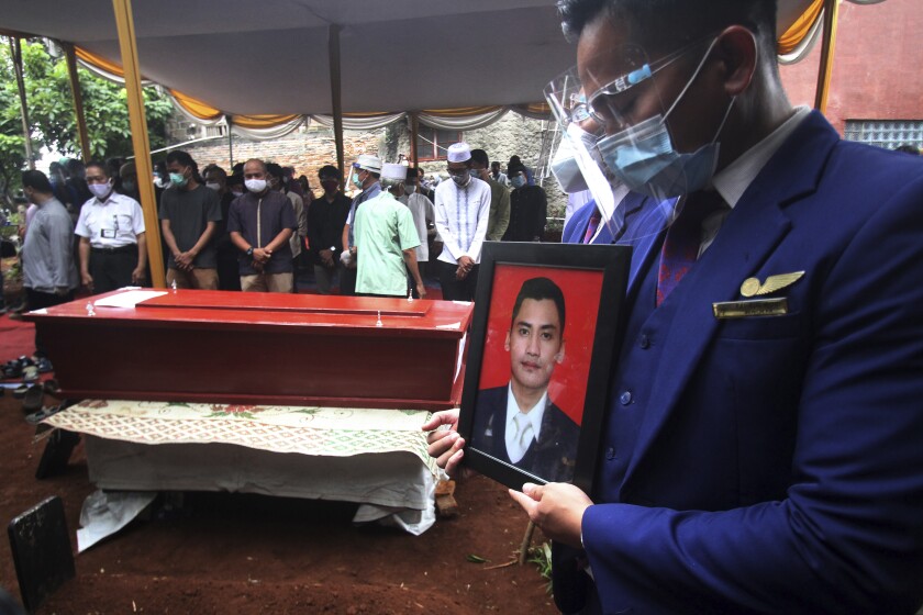 A colleague holds a portrait of Okky Bisma, a flight steward, one of victims of the crashed Sriwijaya Air passenger jet during his funeral in Jakarta, Indonesia.Thursday, Jan. 14, 2021. An aerial search for victims and wreckage of the crashed Indonesian plane expanded Thursday as divers continued combing the debris-littered seabed looking for the cockpit voice recorder from the lost Sriwijaya Air jet. (AP Photo)