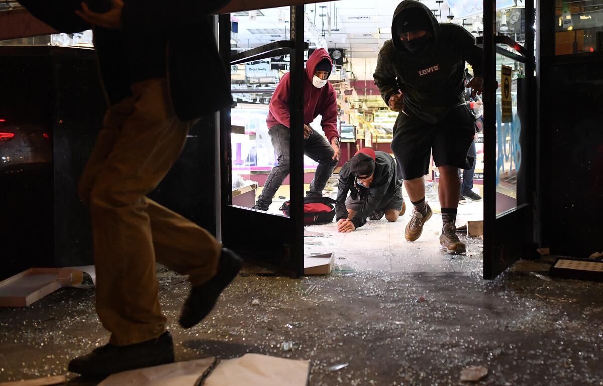 Looters run from a jewelry store as LAPD officers approach in downtown Los Angeles Friday night.