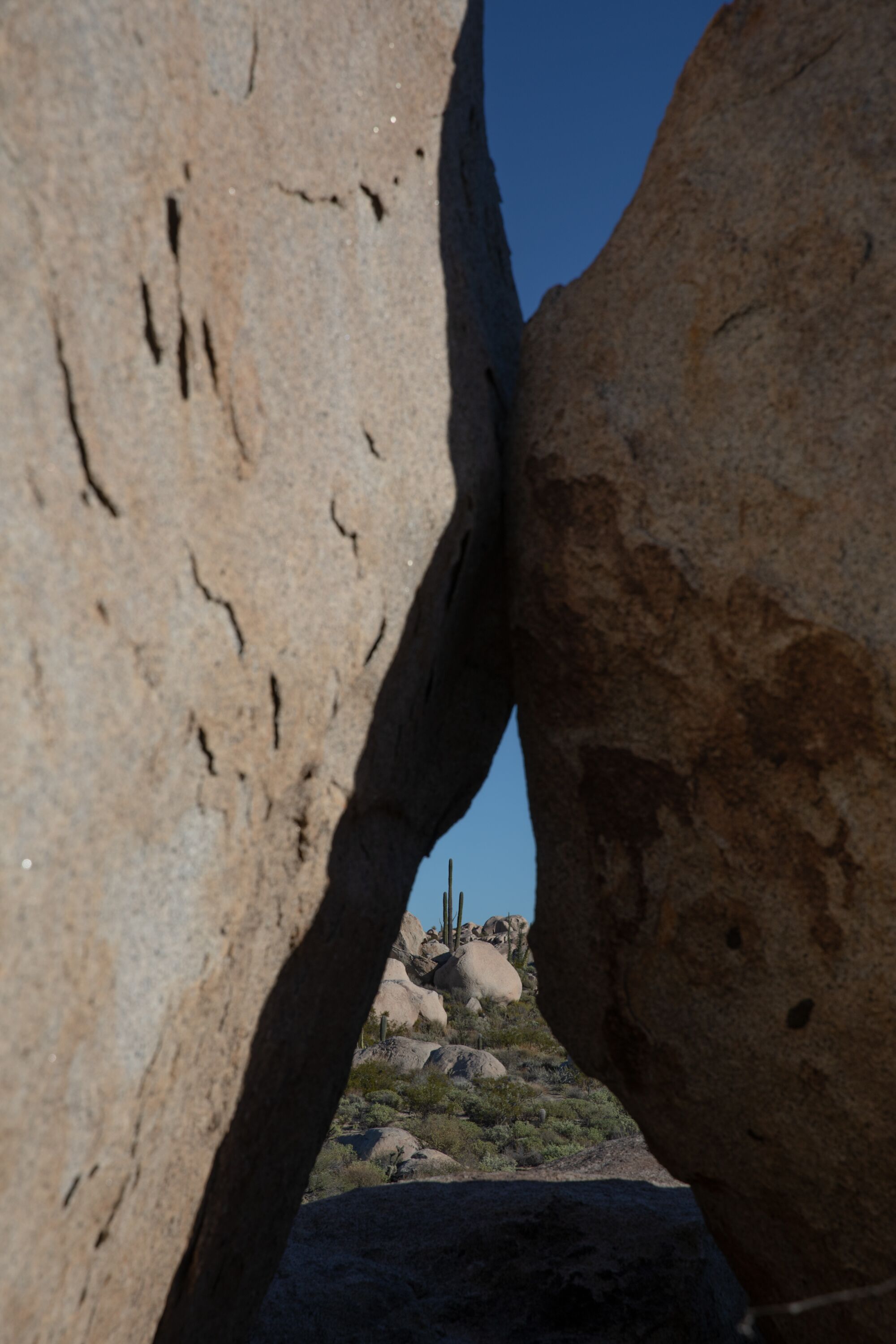 Two large boulders in the foreground frame another set of boulders and a cactus in the background