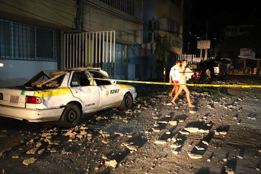 Una pareja pasa junto a un taxi que resultó dañado por la caída de escombros después de un fuerte terremoto en Acapulco, México.